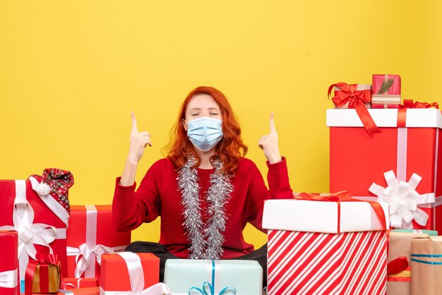 Front view pretty female sitting around presents in mask on a yellow 