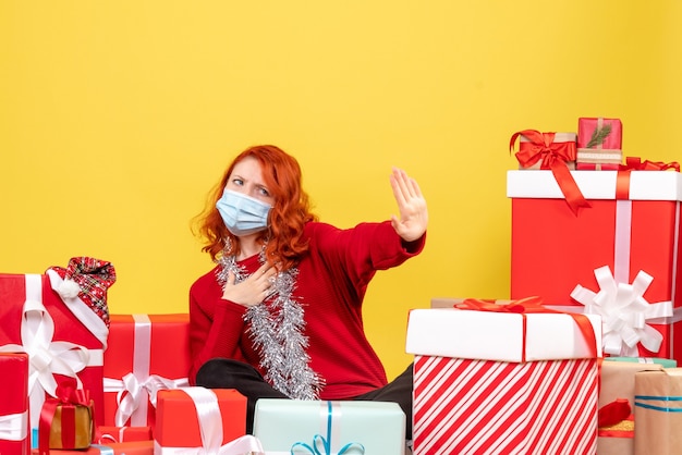 Front view pretty female sitting around presents in mask on a yellow 