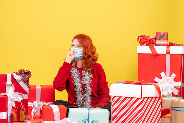 Front view pretty female sitting around presents in mask on a yellow 