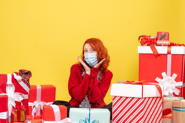 Front view pretty female sitting around presents in mask on the yellow 