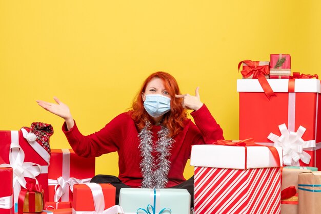 Front view pretty female sitting around presents in mask on the yellow 