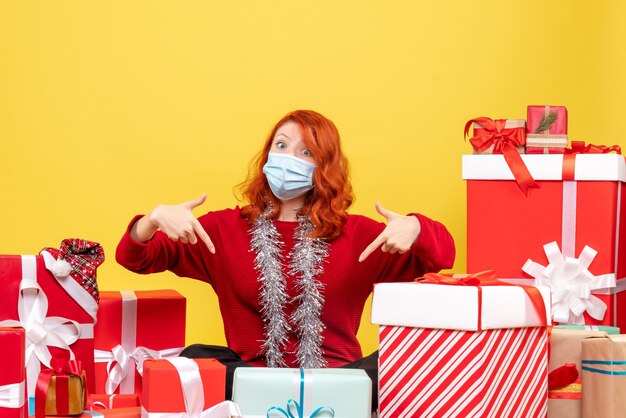 Front view pretty female sitting around presents in mask on the yellow 