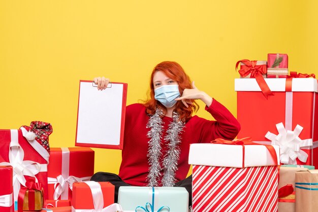 Front view pretty female sitting around presents in mask on yellow 