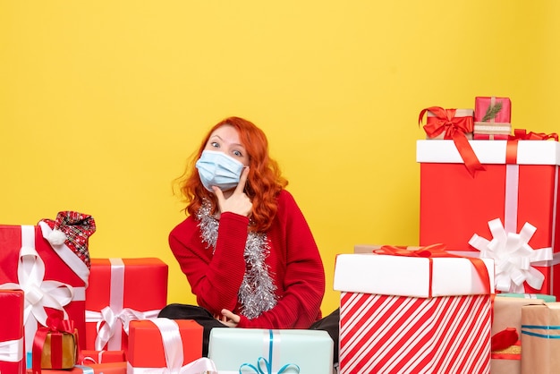 Front view pretty female sitting around presents in mask on yellow 