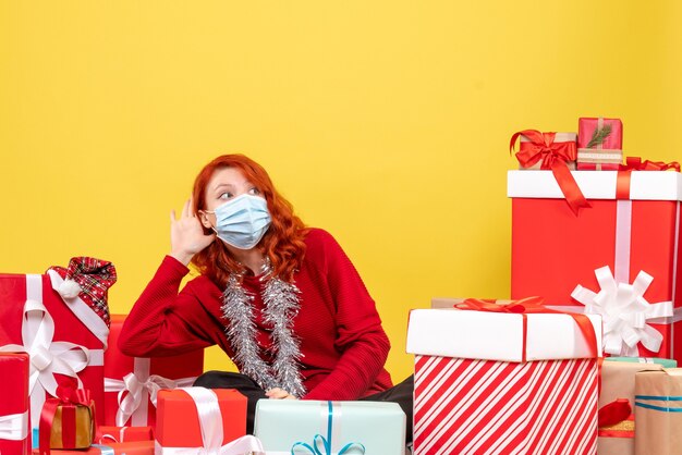 Front view pretty female sitting around presents in mask on yellow 