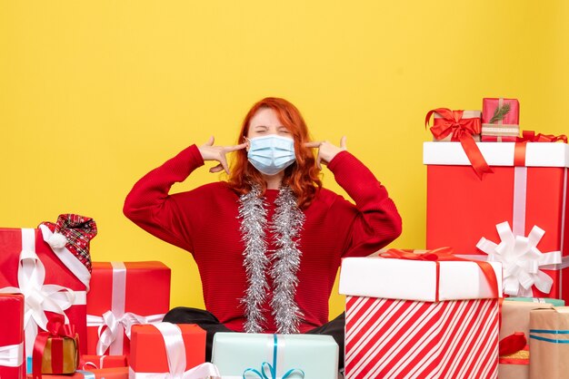 Front view pretty female sitting around presents in mask on yellow 