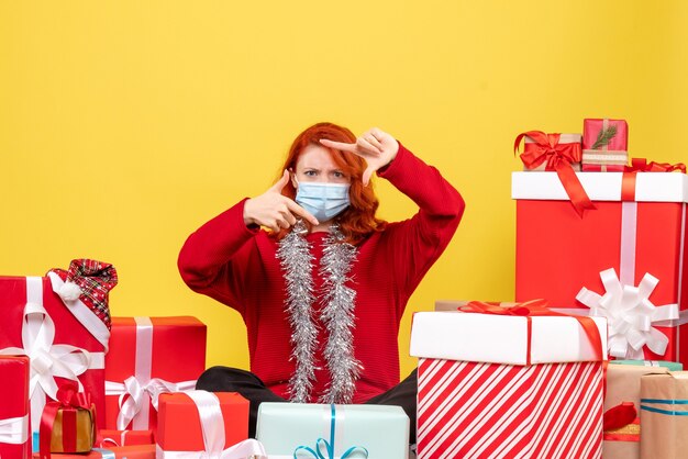 Front view pretty female sitting around presents in mask on yellow 