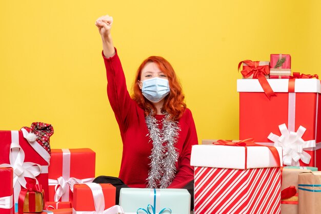 Front view pretty female sitting around presents in mask on yellow 