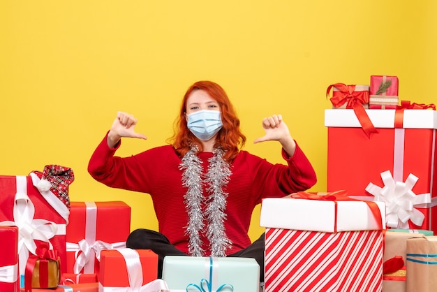 Front view pretty female sitting around presents in mask on yellow 