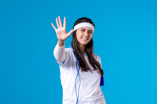 Вид спереди красивая женщина в спортивной одежде со скакалкой на синем
