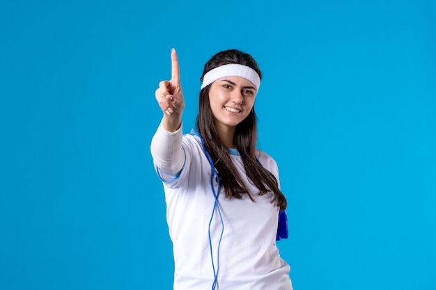 Front view pretty female in sport clothes with skipping rope on blue 