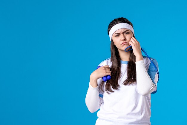 Front view pretty female in sport clothes with skipping rope on blue 