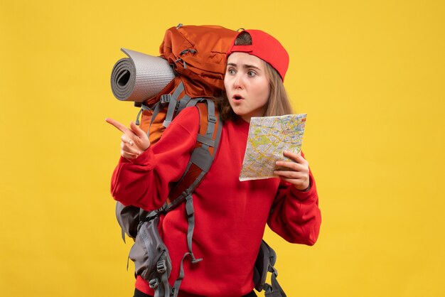 Front view pretty female traveler with backpack holding map pointing at left