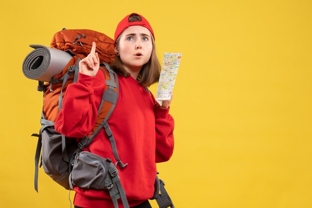 Front view pretty female traveler with backpack holding up map pointing at ceiling