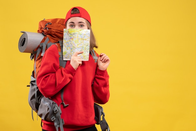 Front view pretty female traveler with backpack holding up travel map to her face