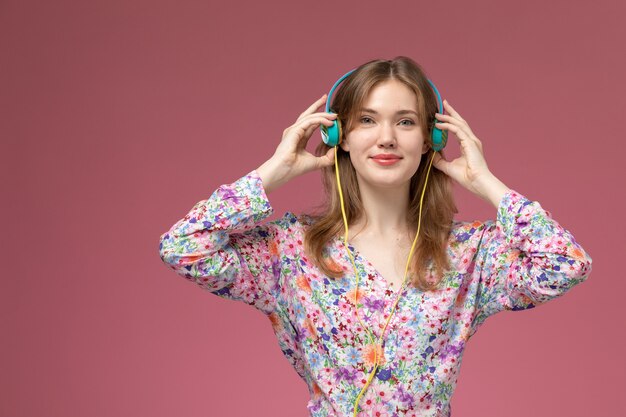 Front view pretty lady putting on her headphone on dark pink wall