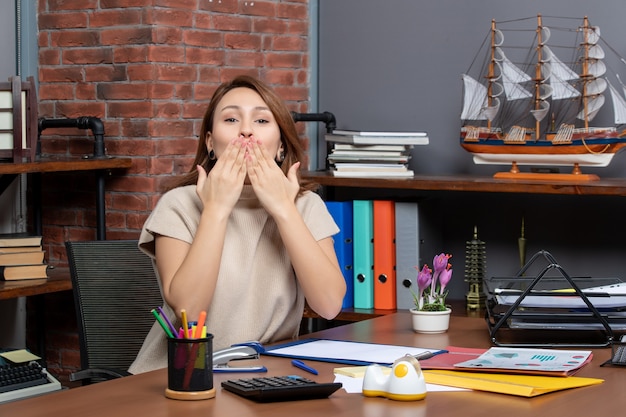 Front view of pretty woman blowing a kiss working in office