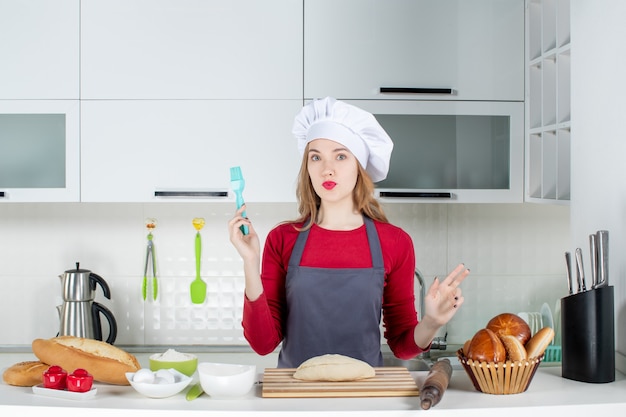 Вид спереди красивая женщина в шляпе повара, держащая кисть на кухне