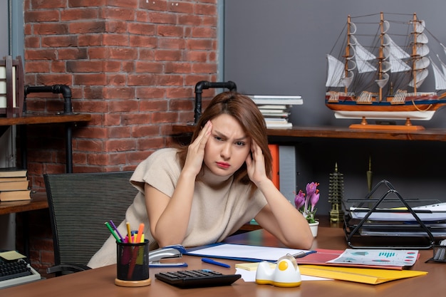 Front view of pretty woman holding her head with pain working in office