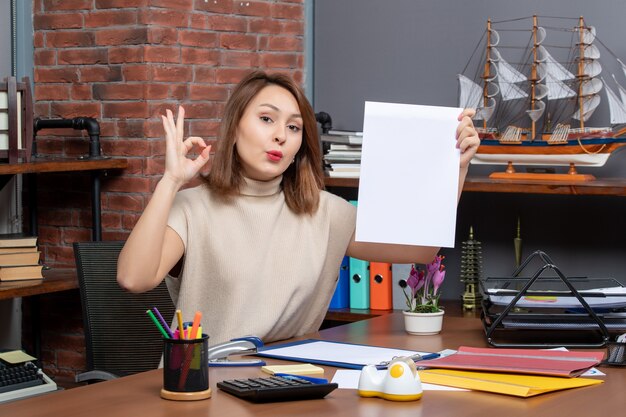 Front view of pretty woman making okey sign sitting at wall