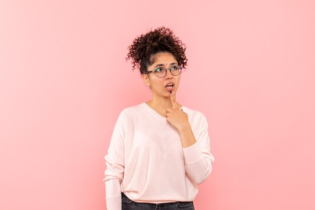 Front view of pretty woman thinking on pink wall