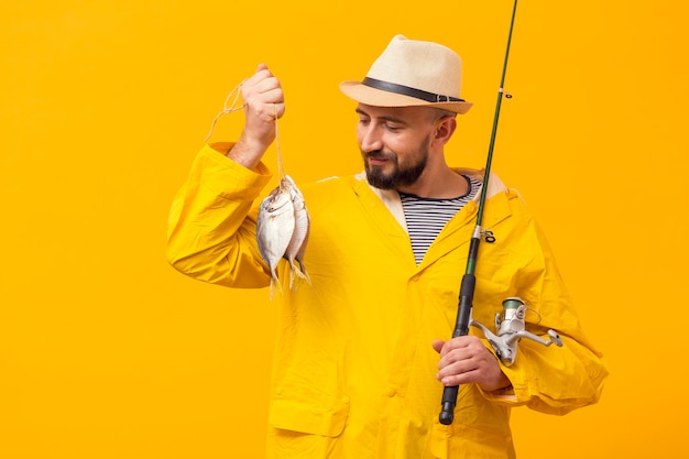 Foto gratuita vista frontale del pescatore fiero che tiene fermo e canna da pesca