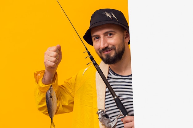 Front view of proud fisherman holding fishing rod with catch