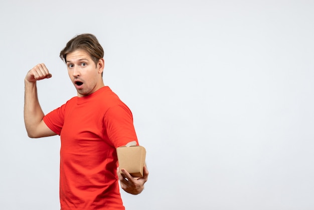 Вид спереди гордого молодого парня в красной блузке, держащего коробочку на белом фоне