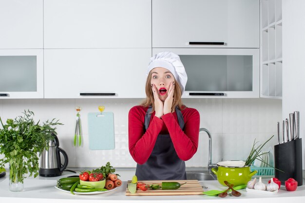 Front view puzzled female cook in apron standing in kitchen