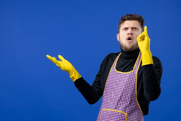 Front view of puzzled housekeeper man looking at ceiling on blue wall