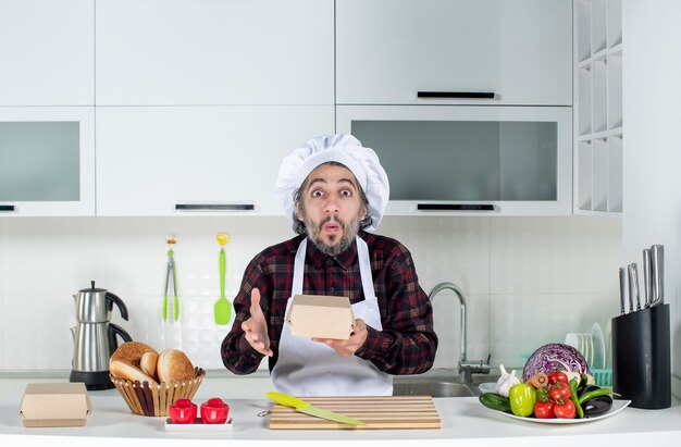 Вид спереди озадаченного шеф-повара в униформе, держащего коробку на кухне