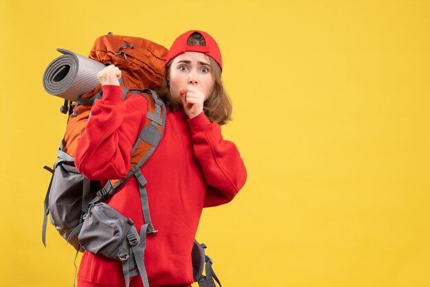 正面図困惑した旅行者の女性が黄色い壁に立っている赤いバックパックで