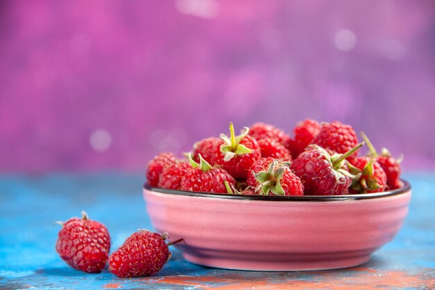 Front view raspberries in a bowl on blue table pink table free space