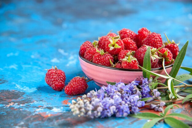 Front view raspberries in a bowl purple flowers on blue table free place