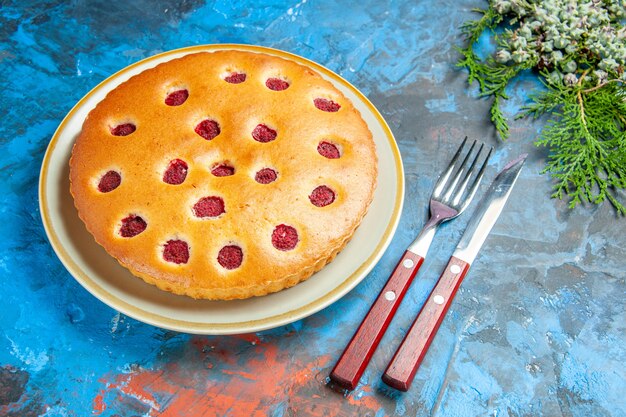 Torta al lampone vista frontale sul coltello forchetta coni piatto ovale sul tavolo blu