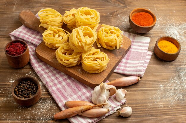 Free photo front view raw dough flower formed pasta with seasonings on a wooden space