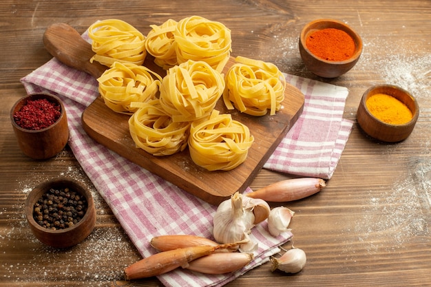 Front view raw dough flower formed pasta with seasonings on a wooden space