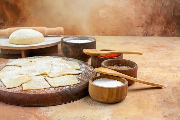 Вид спереди кусочки сырого теста с мукой и приправами на сливочном столе, блюдо, паста