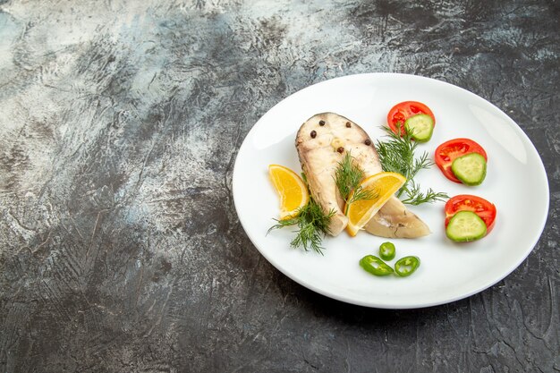 空きスペースのある灰色の氷の表面の左側にある白い皿に生の魚と唐辛子の生鮮食品の正面図