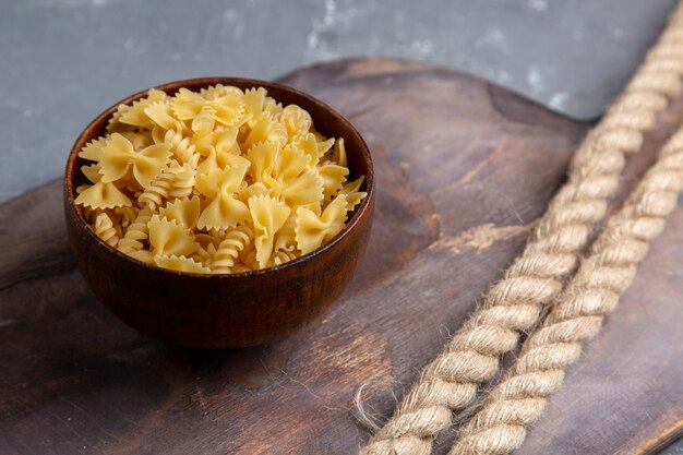 Foto gratuita una pasta italiana cruda di vista frontale poco formata all'interno del piatto marrone sul pasto italiano dell'alimento della pasta da tavola marrone