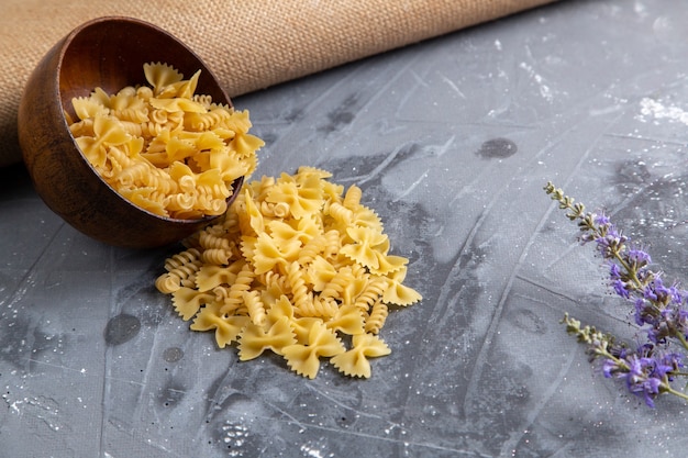 Foto gratuita una pasta italiana cruda di vista frontale poco formata all'interno del piatto marrone sulla foto grezza del pasto italiano della pasta da tavola grigia