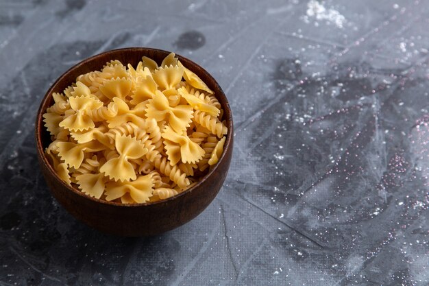 A front view raw italian pasta little formed inside brown plate on the grey table pasta italian food meal