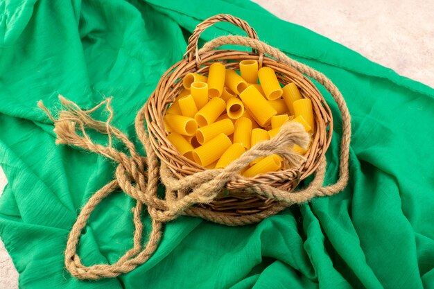 Вид спереди сырые итальянские макароны, желтые внутри маленькой корзины вместе с веревками на зеленой ткани
