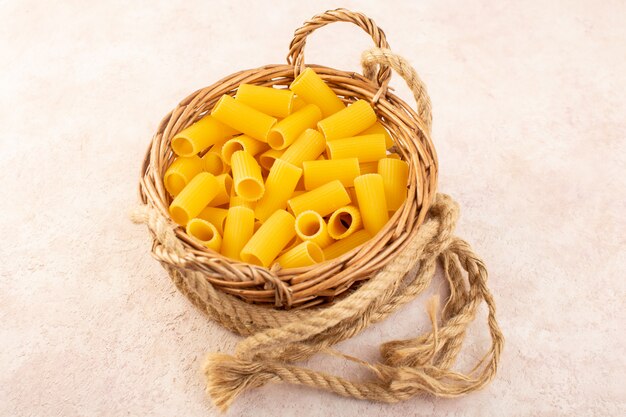 A front view raw italian pasta yellow inside little basket along with ropes on pink