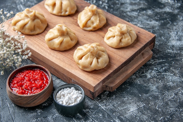 Front view raw little dumplings with meat on a dark surface flour color dough cooking board meal dish meat pepper