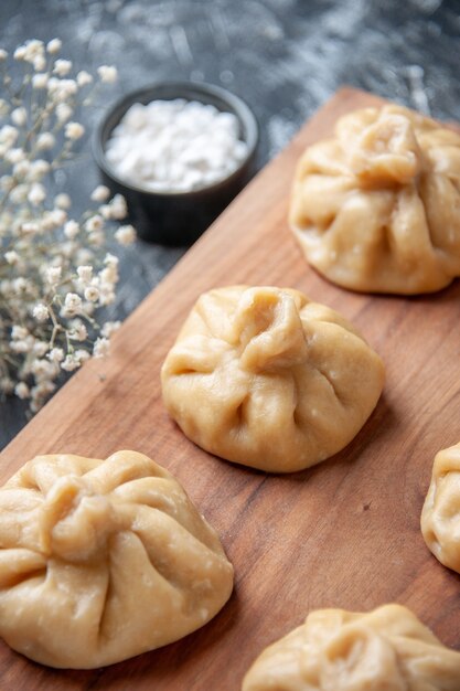 正面図生の小さな餃子と暗い表面の小麦粉色生地ペッパークッキングボード食事皿肉