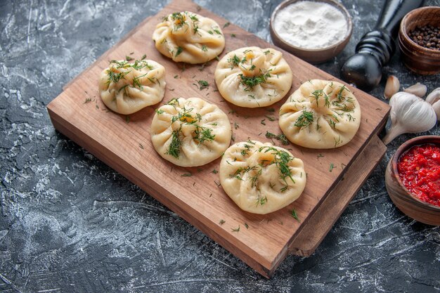 Вид спереди сырые маленькие пельмени с мясом и томатным соусом на серой поверхности мука из теста торт пирог кухня блюдо ужин приготовление мяса