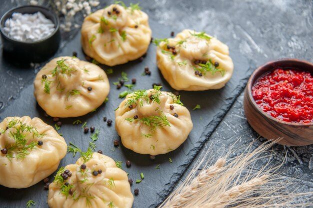 Front view raw little dumplings with tomato sauce and garlic on light-gray surface meat cuisine meal dinner cake dough cooking dish