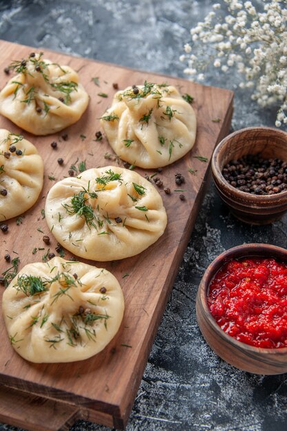 Front view raw little dumplings with tomato sauce and seasonings on a gray surface meat dough meal cake cooking dish cuisine dinner