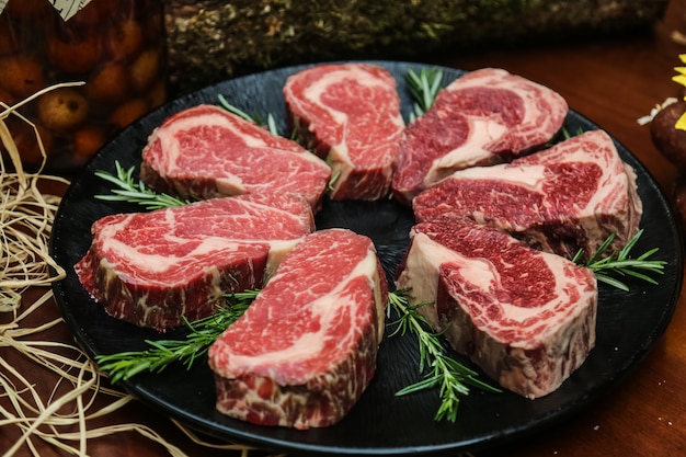 Foto gratuita vista frontale carne marmorizzata cruda per bistecca con rosmarino su un supporto